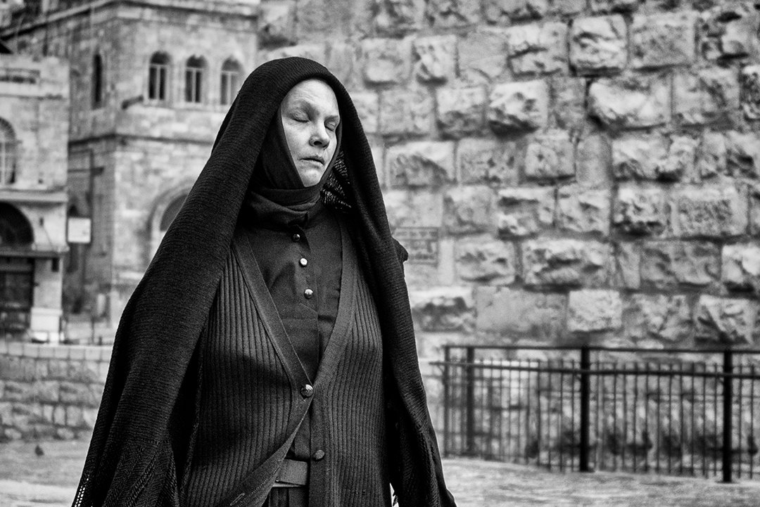 A woman wearing a dark veil beside a stone wall.